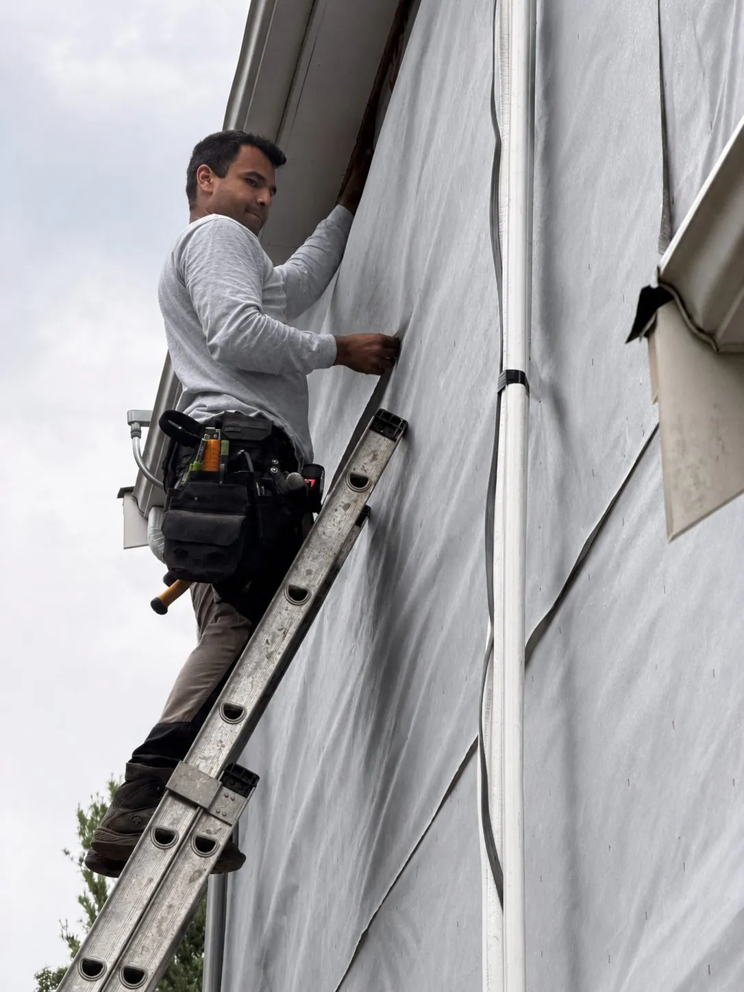 Vitor Cavallari, owner of Redline Carpentry, installing siding on a ladder